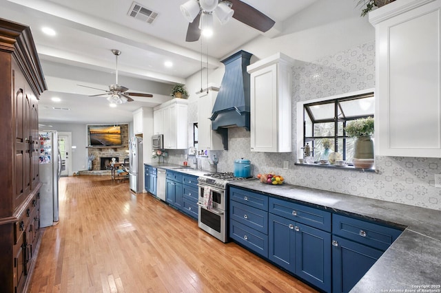 kitchen with blue cabinets, stainless steel appliances, ceiling fan, premium range hood, and beamed ceiling