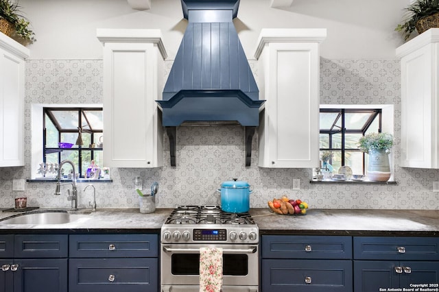kitchen with stainless steel gas range, a sink, premium range hood, blue cabinetry, and white cabinets
