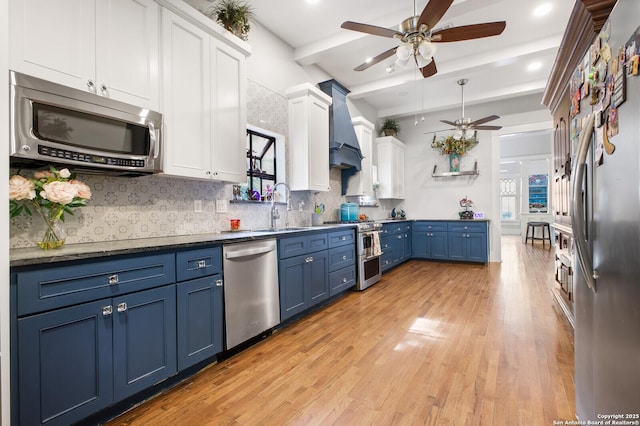 kitchen with stainless steel appliances, blue cabinets, a ceiling fan, a sink, and custom range hood