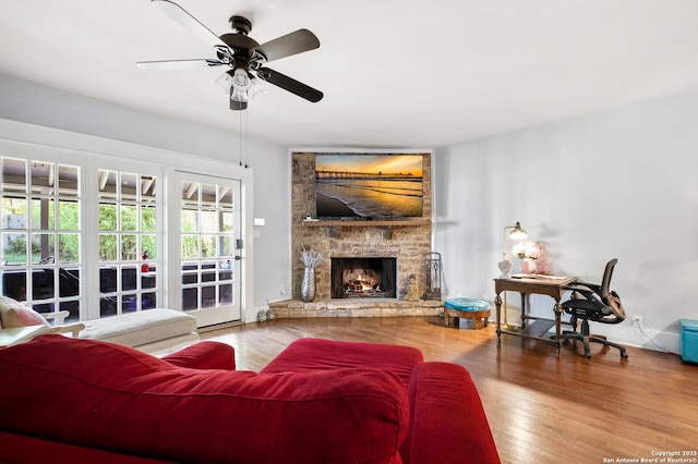living area with a stone fireplace, ceiling fan, and wood finished floors