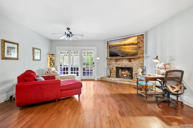living room with wood-type flooring, ceiling fan, a fireplace, and baseboards
