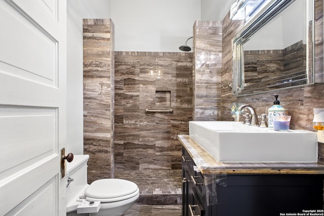 full bath with vanity, a tile shower, toilet, and tile walls