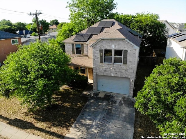 view of front of house featuring brick siding, a garage, driveway, solar panels, and fence