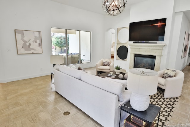 living room featuring a chandelier, arched walkways, a glass covered fireplace, and baseboards
