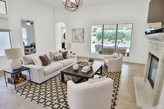 living area with a premium fireplace, arched walkways, a high ceiling, baseboards, and a chandelier