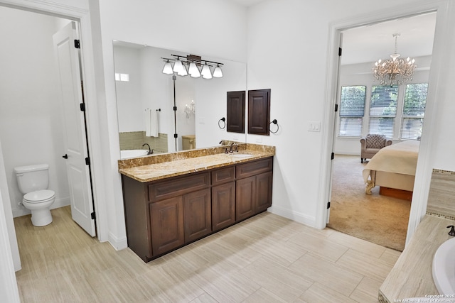 bathroom with toilet, a chandelier, a bath, vanity, and baseboards