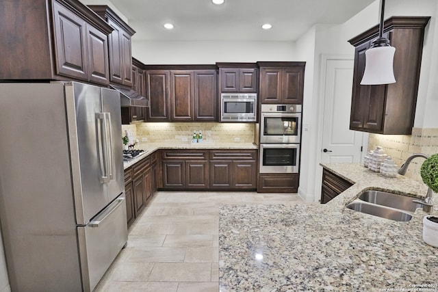 kitchen with appliances with stainless steel finishes, a sink, decorative backsplash, dark brown cabinetry, and light stone counters