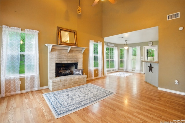 unfurnished living room with baseboards, wood finished floors, a fireplace, a ceiling fan, and a high ceiling