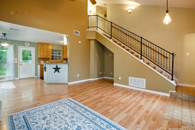 unfurnished living room featuring light wood-style floors, a towering ceiling, baseboards, a ceiling fan, and stairs