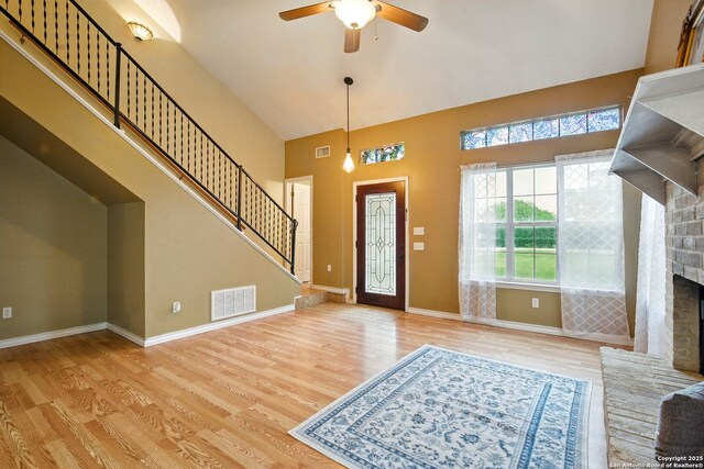 foyer with a brick fireplace, wood finished floors, ceiling fan, a towering ceiling, and baseboards