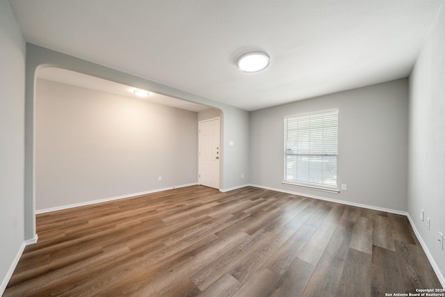 spare room featuring arched walkways, wood finished floors, and baseboards