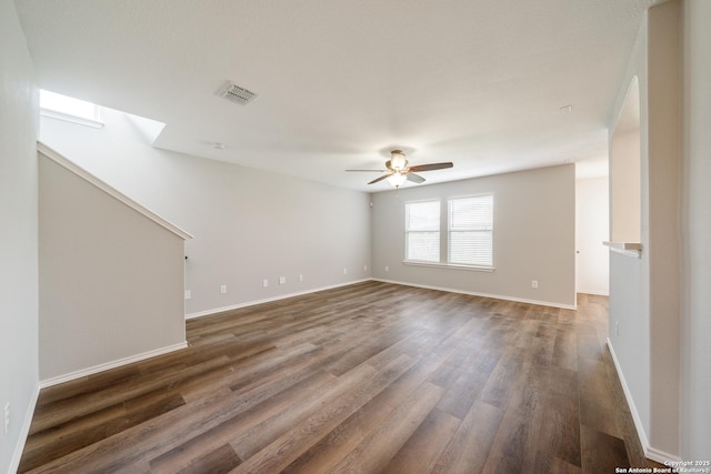 empty room featuring a ceiling fan, dark wood-type flooring, baseboards, and a skylight