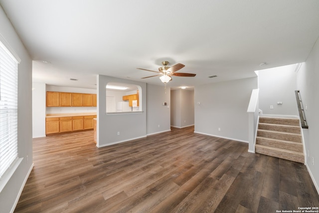 unfurnished living room with ceiling fan, dark wood-type flooring, baseboards, and stairs