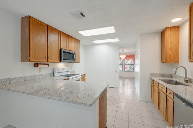 kitchen featuring stainless steel appliances, a sink, a skylight, light stone counters, and a peninsula