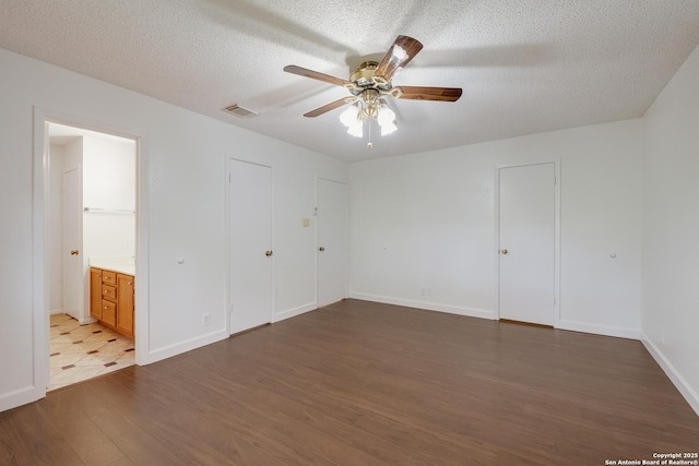unfurnished bedroom with wood finished floors, a textured ceiling, baseboards, ensuite bath, and ceiling fan