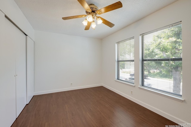 unfurnished bedroom featuring dark wood finished floors, multiple windows, a closet, baseboards, and a textured ceiling