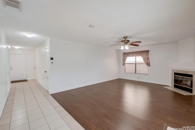 unfurnished living room featuring a ceiling fan, a textured ceiling, wood finished floors, a fireplace, and baseboards
