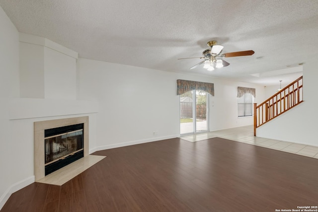 unfurnished living room featuring a ceiling fan, a fireplace with flush hearth, a textured ceiling, wood finished floors, and stairway