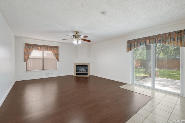 unfurnished living room featuring ceiling fan, wood finished floors, a textured ceiling, a fireplace, and baseboards