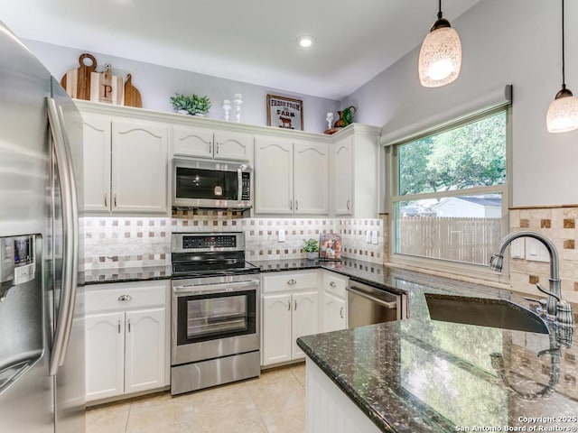 kitchen featuring stainless steel appliances, a sink, white cabinets, dark stone countertops, and decorative backsplash