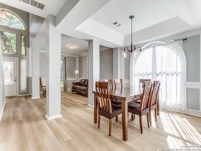 dining room featuring a chandelier, healthy amount of natural light, light wood-style flooring, and a raised ceiling