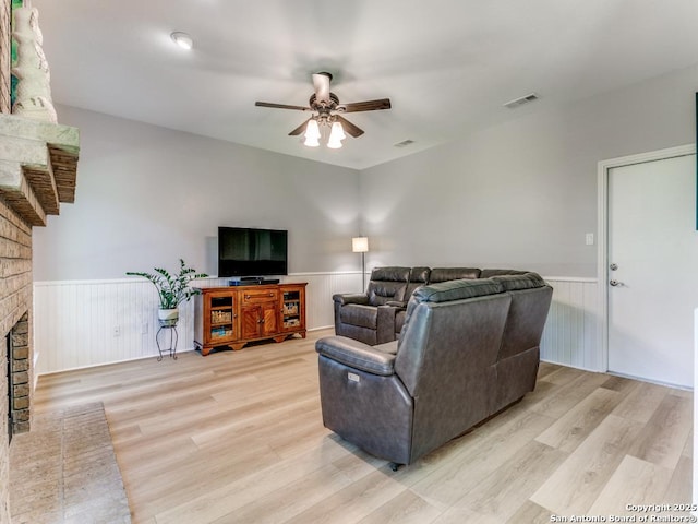 living area featuring a wainscoted wall, a ceiling fan, light wood-type flooring, and a fireplace