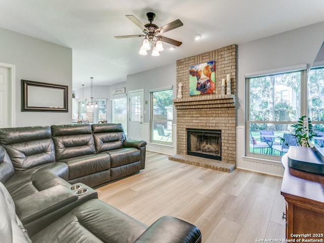 living area with ceiling fan, healthy amount of natural light, light wood finished floors, and a brick fireplace