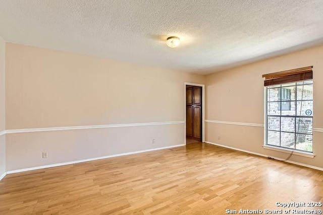 empty room featuring light wood-style flooring, a textured ceiling, and baseboards