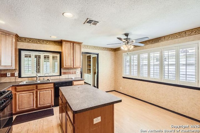 kitchen featuring a sink, black appliances, light wood finished floors, a center island, and a textured ceiling