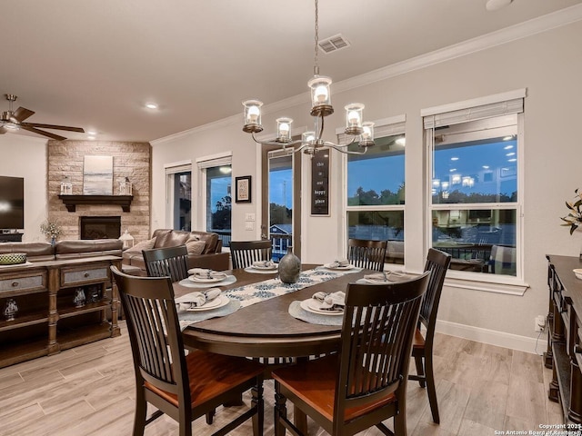 dining area with a ceiling fan, light wood finished floors, crown molding, a stone fireplace, and a chandelier
