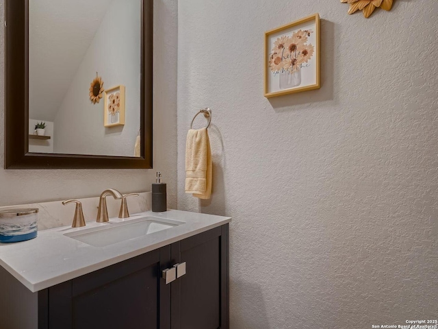 bathroom with a textured wall, vanity, and lofted ceiling