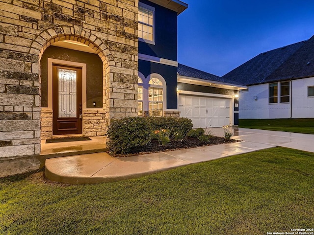 entrance to property featuring stone siding, a lawn, driveway, and an attached garage