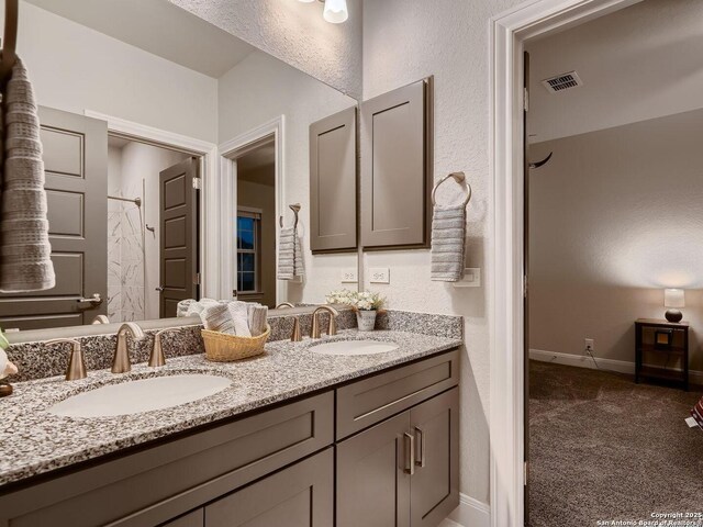 bathroom featuring double vanity, a textured wall, baseboards, and a shower