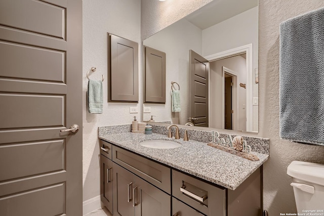 bathroom with a textured wall, toilet, and vanity