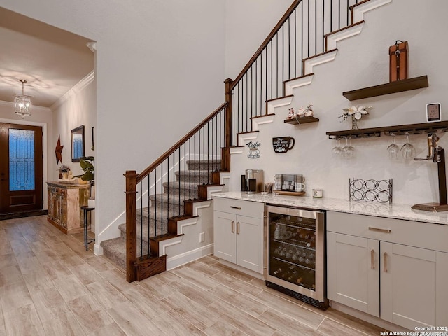 indoor dry bar featuring beverage cooler, stairway, ornamental molding, light wood-style flooring, and a chandelier
