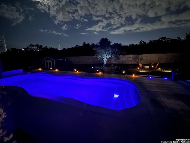 pool at night featuring an outdoor fire pit, a jacuzzi, and a patio