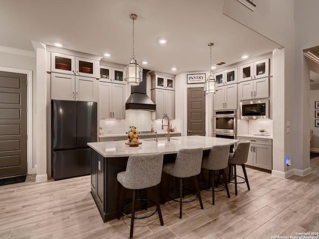 kitchen featuring stainless steel appliances, a sink, custom exhaust hood, a kitchen island with sink, and backsplash