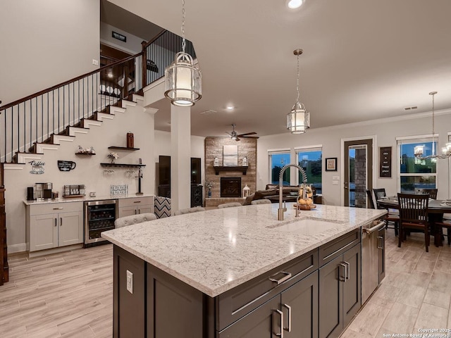 kitchen with beverage cooler, a sink, ceiling fan, a stone fireplace, and light stone counters