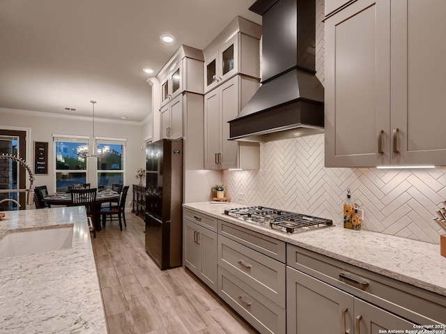 kitchen featuring wall chimney exhaust hood, freestanding refrigerator, stainless steel gas stovetop, a sink, and backsplash