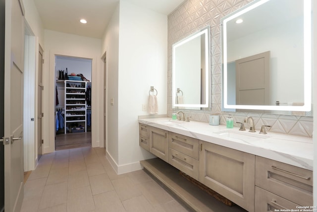 full bath featuring decorative backsplash, double vanity, a walk in closet, baseboards, and recessed lighting
