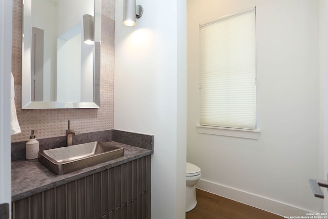 bathroom with toilet, baseboards, decorative backsplash, wood finished floors, and vanity