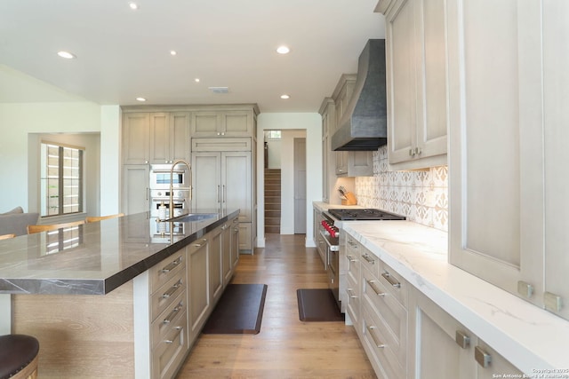 kitchen with stainless steel appliances, wall chimney exhaust hood, light wood-style floors, tasteful backsplash, and light stone counters