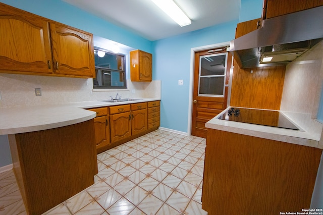 kitchen with under cabinet range hood, black electric cooktop, a sink, brown cabinetry, and light countertops