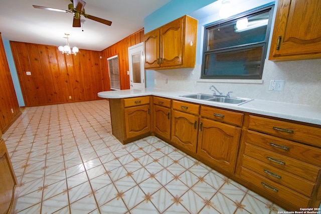 kitchen with a sink, a peninsula, wood walls, brown cabinetry, and light flooring