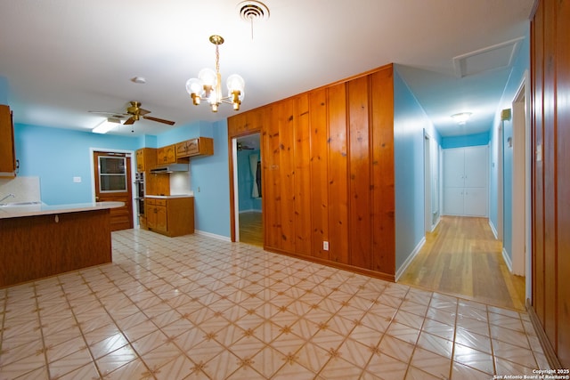 kitchen with under cabinet range hood, light countertops, brown cabinetry, baseboards, and a peninsula