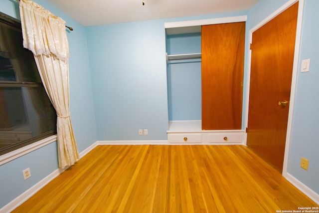 unfurnished bedroom with wood finished floors, baseboards, and a closet