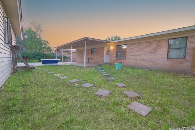 back of property at dusk featuring a patio area, a yard, and brick siding