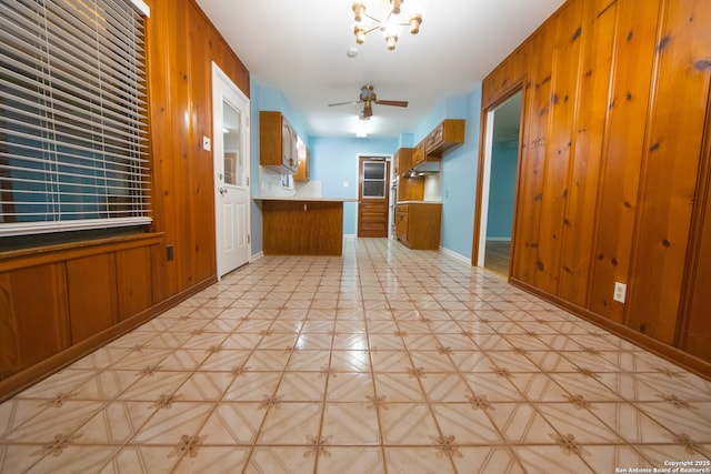 kitchen featuring brown cabinetry, wood walls, a peninsula, baseboards, and ceiling fan