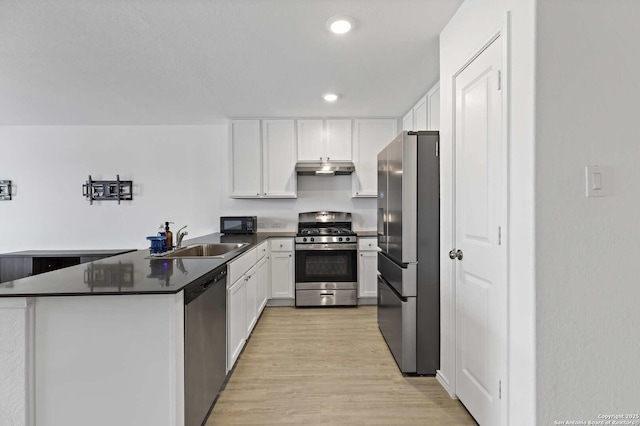 kitchen with appliances with stainless steel finishes, a sink, white cabinets, light wood finished floors, and dark countertops