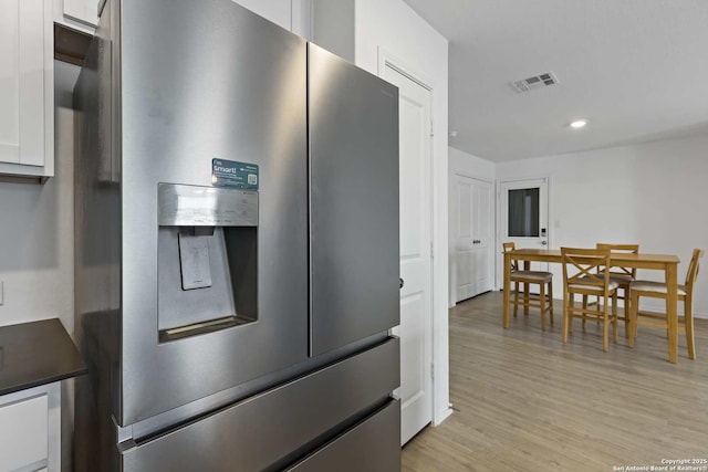 kitchen featuring stainless steel refrigerator with ice dispenser, white cabinetry, light wood-style flooring, dark countertops, and recessed lighting